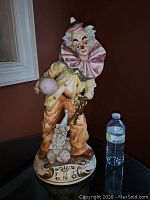 Full view of 20 inch Capodimonte clown figurine standing next to water bottle for scale on black surface