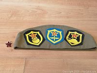Soviet military side cap with three embroidered patches on a wooden floor.