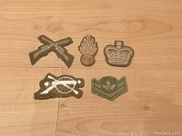 Group of 5 vintage military patches laid out on a wood surface, showing crossed rifles, grenade, crown, crossed cannons and maple leaf chevron
