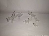 Group of six small frosted art glass elephant figurines captured on white background showing size variation and trunk positions.
