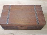 Top view of rectangular wooden box showing two dark inlay strips on the lid and some surface wear.
