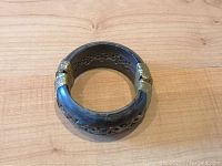 Top view of carved ebony bracelet showing full circular shape with carved cutouts and brass accents on wood surface.
