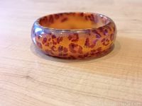 Front and side views of a translucent amber bakelite bangle bracelet with embedded gold leaf leopard print design. Photos show the smooth glossy surface and rounded edges.