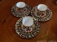 Three complete trios arranged on table, showing cups, saucers and plates with Imari-style pattern