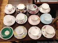 Overview of all twelve cups and saucers laid out on a wooden table showing varied designs and colors.