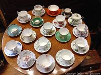 Eighteen assorted vintage cups and saucer sets arranged on a table showing various floral and patterned designs.