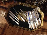 Overall view of knife set on decorative tray, showing mother of pearl handles and blades