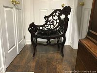 Side view of occasional chair showing intricate carved wooden backrest and armrest design with pedestal legs.