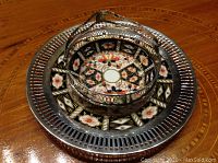 Top view of two Imari pattern plates mounted in sterling silver, one with basket handle, one plain