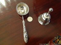 Top view of serving spoon showing detailed sterling handle, pierced bowl, and quarter coin for size reference, next to the silver plate dinner bell.