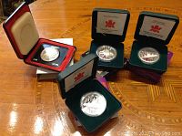 Four Canadian silver dollar coins in four separate mint presentation boxes arranged on a wooden surface.