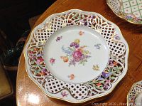Front of plate with central pink, purple and orange floral bouquet on reticulated lattice rim with gold trim