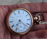 Dial side of pocket watch held in hand showing white enamel dial with Roman numerals and subsidiary seconds