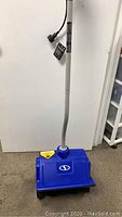 Full view of Snow Joe electric snow shovel standing upright showing blue plastic head and handle.