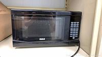 Front view showing black RCA microwave oven with windowed door and RCA logo.