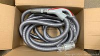 Central vacuum hose coiled inside a cardboard box
