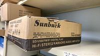 Original box with Sunbuck branding and model number TAV-6188BT, showing shipping wear and details of the karaoke amplifier.