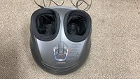 Front view of the foot massager showing foot compartments and control panel on a carpeted floor.