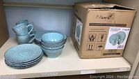 Photo showing the full set of ceramic dinnerware including the boxed packaging with product details and the stacked dishes and cups.