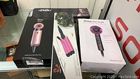 Boxed hair appliances including Breeze hair dryer, Dodo hair dryer, and curling iron boxes displayed on glass surface.