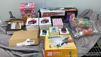 Wide view of the lot showing all items including the boxed Racing Boat, 3D pen box, kids watches, Hatchimals Pixies, and Batman light with accessories.