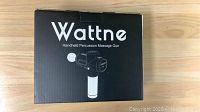 Box front showing Wattne branding and illustration of the handheld percussion massage gun.