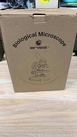 Closed cardboard box labeled 'Biological Microscope Bnise' with microscope illustration.