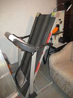 Side view of the treadmill folded upright showing the belt, frame, and handlebar design.