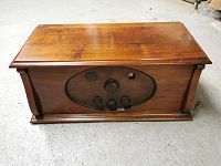 Front view of wooden cabinet radio with oval speaker grille, tuning dial window, and three control knobs