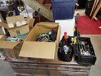 Multiple boxes on a plastic-wrapped table including cardboard boxes with books and two black plastic toolboxes along with a soft tool bag containing tools