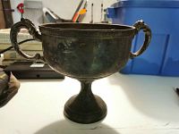 Front view of silver plated two-handled urn showing handles, cup shape, and pedestal base with tarnished surface.