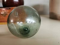 Side view of the pale green translucent glass fishing float showing round shape with bubbles inside the glass and smooth surface.