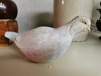 Side view of the carved wooden bird figurine, showing the rounded body and tail with faded white and grey paint.
