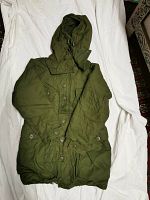 Full view of green Canadian military parka with attached hood and button closure laid flat on white sheet.