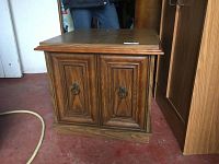 Front view of the oak end table showing two paneled cabinet doors with dark metal ring pull handles and wood grain finish.