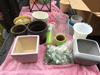 Multiple ceramic and glass planters and vases arranged on pink cloth with a bag of vase stones and a clear plastic bottle