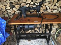 Full side view of the industrial Singer sewing machine mounted on wooden tabletop with motor attached underneath, showing heavy cast iron base and machine arm with wheel.