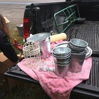 Basket contents placed on pink cloth on truck tailgate, showing plastic hangers, metal pots, decorative bird cage, candle