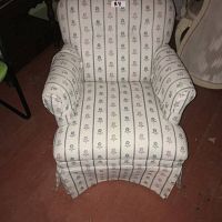 Front view of the small upholstered armchair showing floral striped fabric, padded arms, and skirted bottom.