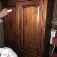 Front view of the wooden entertainment centre showing the two paneled doors, metal knobs, and maple stain finish.