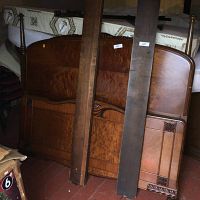 Antique wooden bed frame components including headboard, footboard, and side rails leaning against a wall in storage environment.
