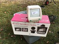 Small white CRT monitor placed on top of the original box, outdoors on grass, showing front and side views