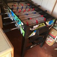 Foosball table with red and blue figurines on rods, black frame with colorful graphics, and manual scoring counter.