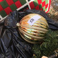 Close-up of gold-tone ribbed and glittery Christmas ball ornament on black plastic and part of carpet visible