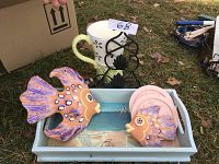 Set of two ceramic fish, coasters, tray, serviette holder, and pitcher arranged on ground with grass background