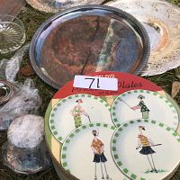 Photo showing Gold Club porcelain plates with stylized female illustrations and two silver serving trays on grass