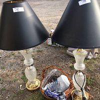 Pair of cut glass lamps with brass-colored bases and black lampshades with brass-colored linings, standing outside on ground.