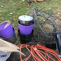 Coiled thick black cable wire, orange extension cord, and several small metal pots with citronella candles inside, some pots painted purple and green