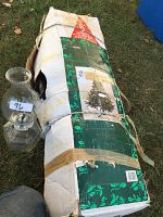 Packed 6 foot artificial Christmas tree in original box secured with tape and twine, box shows some wear and tear from storage and handling.