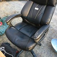 Full view of black leather vinyl desk chair showing wear and peeling on armrests and padded seat and backrest.
